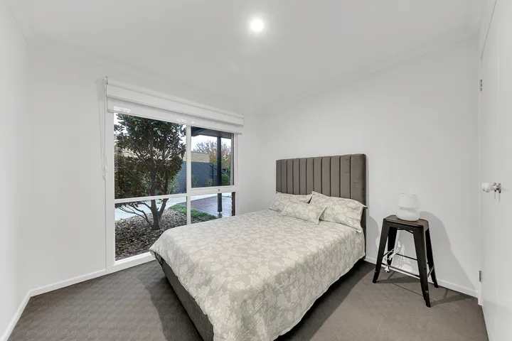 A bedroom at 3 Phelan Drive with a double bed, bedside lamp and a large window looking onto the garden and deck.