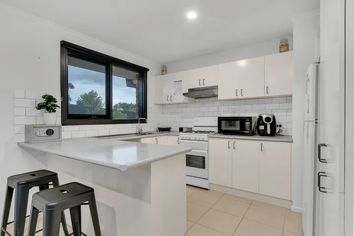 The kitchen at 3 Phelan Drive — white cabinetry, gas cooktop and oven, microwave and air fryer, with a breakfast bar and stools.