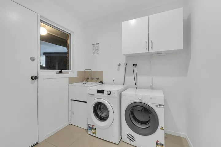 The laundry at 3 Phelan Drive, with a washing machine, dryer, laundry trough and overhead cupboards.