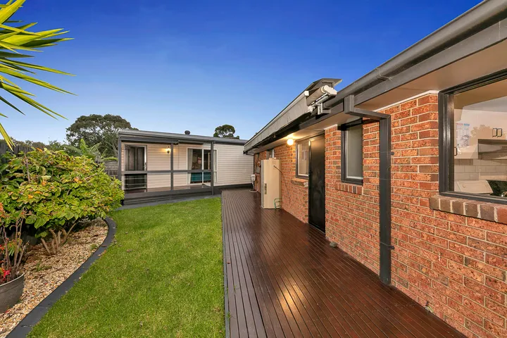 The back garden at 3 Phelan Drive — a timber deck running along the house, lawn, garden beds and a separate outbuilding.