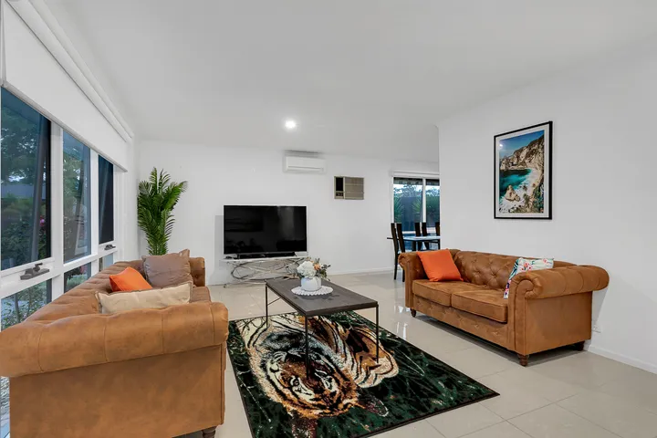 The living room at 3 Phelan Drive, with two sofas facing a television, a rug, and windows onto the garden.